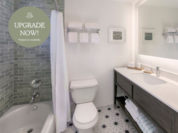 Bright modern bathroom with a bathtub, toilet, sink, towel set, patterned tile floor, and a &ldquo;UPGRADE NOW!&rdquo; promotion circle.