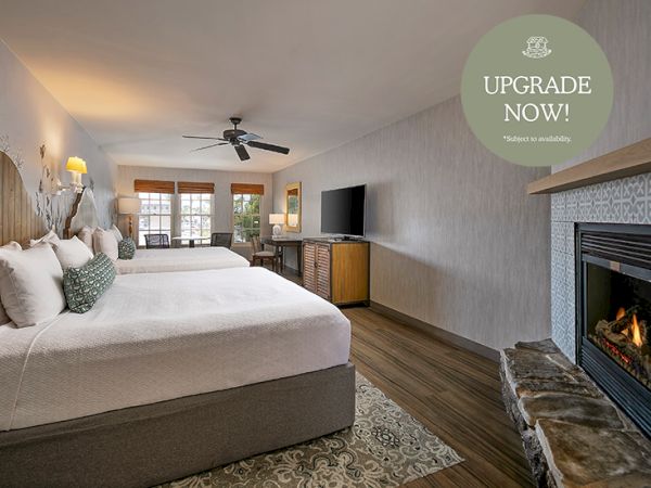 A bright hotel room with a large bed, TV, ceiling fan, desk, and a stone fireplace.