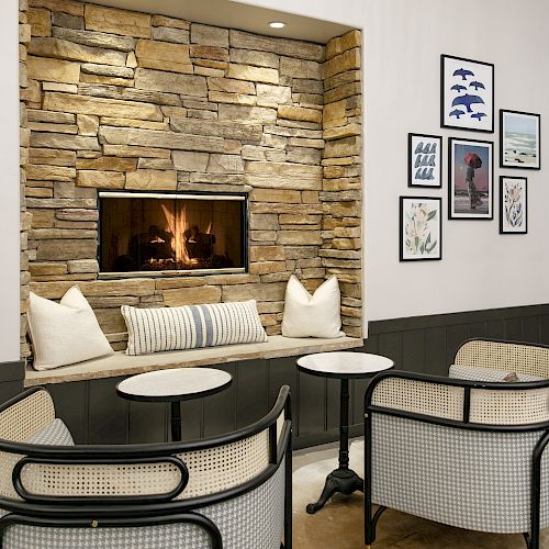 Cozy room with a stone fireplace, framed wall art, and patio-style tables and chairs.