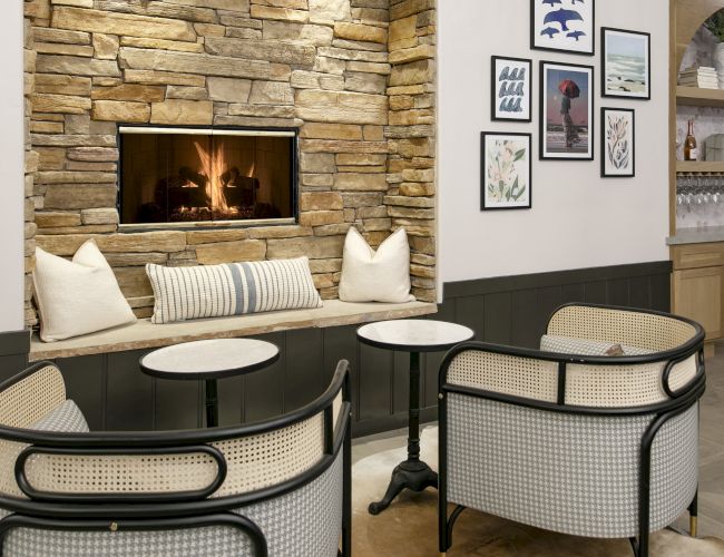 Cozy room with a stone fireplace, framed wall art, and patio-style tables and chairs.