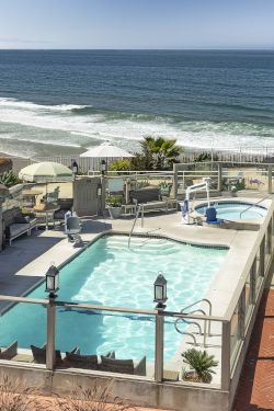 Oceanfront resort patio with turquoise pool, lounge chairs, umbrellas, and a vast blue seascape.