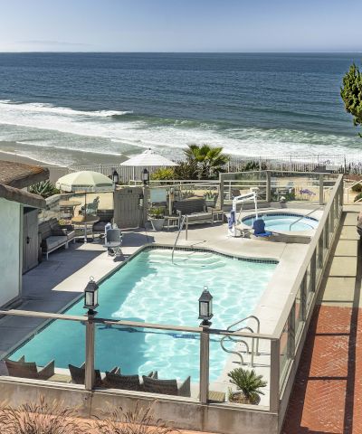 Oceanfront resort patio with turquoise pool, lounge chairs, umbrellas, and a vast blue seascape.