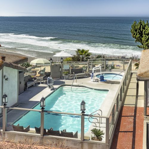 Ocean view from a hotel patio with a turquoise pool, lounge chairs, and umbrellas beside the seaside, inviting you to relax.