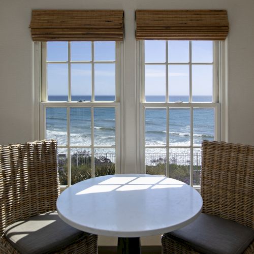 A small round dining table with a white top sits in a cozy wooden nook, flanked by tall windows and wooden chairs, warmly lit.