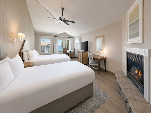 A tidy hotel-style bedroom with two beds, a ceiling fan, a desk with TV, and a stone fireplace.